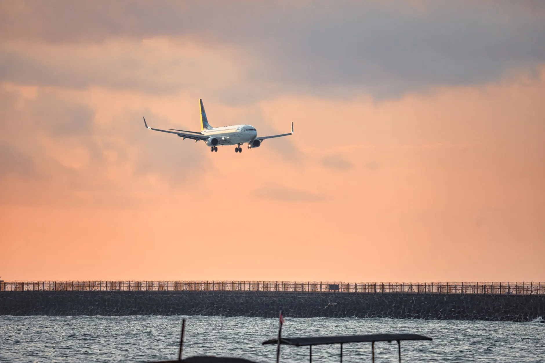 Avion en approche d'un aéroport tropical au coucher du soleil, au-dessus de la mer